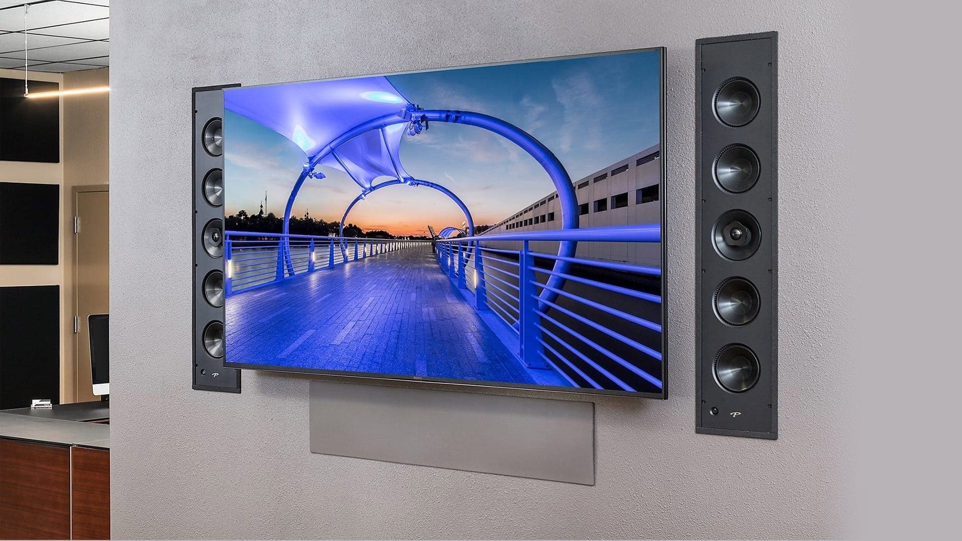 Wall-mounted television flanked by tall in-wall column speakers, with a soundbar mounted beneath