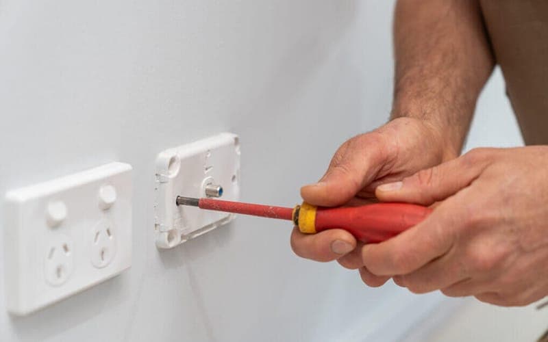 Wall plate being removed with a screwdriver to reach the cabling behind it