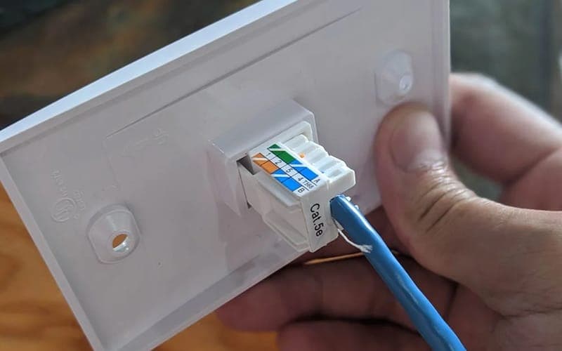 Cat5e cable being plugged into a keystone jack on a data point wall plate