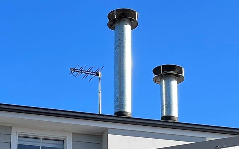 Digital TV antenna mounted beside flue pipes on a rooftop against a clear blue sky
