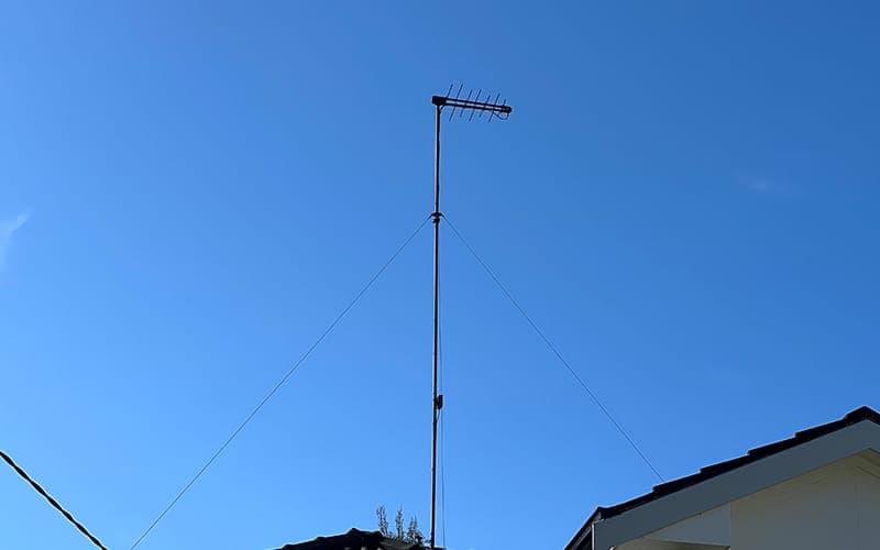 Guyed antenna mast rising above a tiled roof with a digital TV antenna at the top