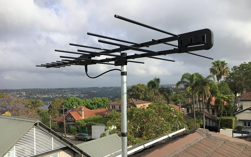 Digital TV antenna with an integrated masthead amplifier on a mast above a suburban rooftop