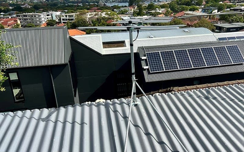 Antenna mast fixed to a corrugated metal roof with coaxial cable run along the ridge