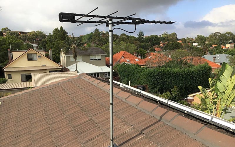 Digital TV antenna installed on a mast above a tiled roof overlooking a suburban valley