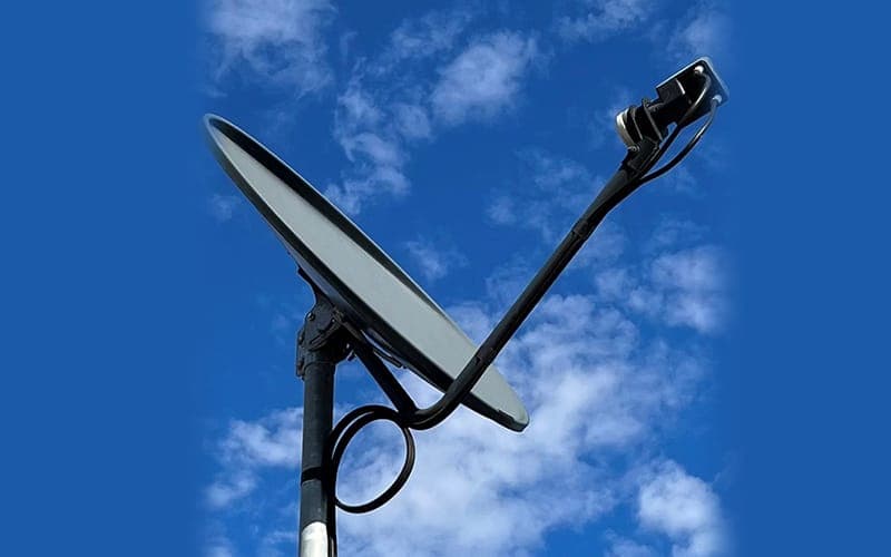 Satellite dish mounted on a pole against a blue sky with a coaxial cable loop