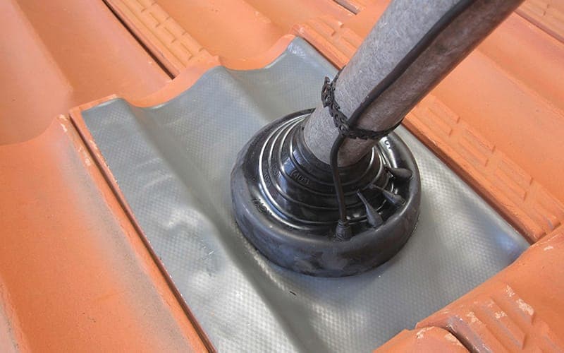 Close-up of a weatherproof flashing boot sealing an antenna mast into a tiled roof