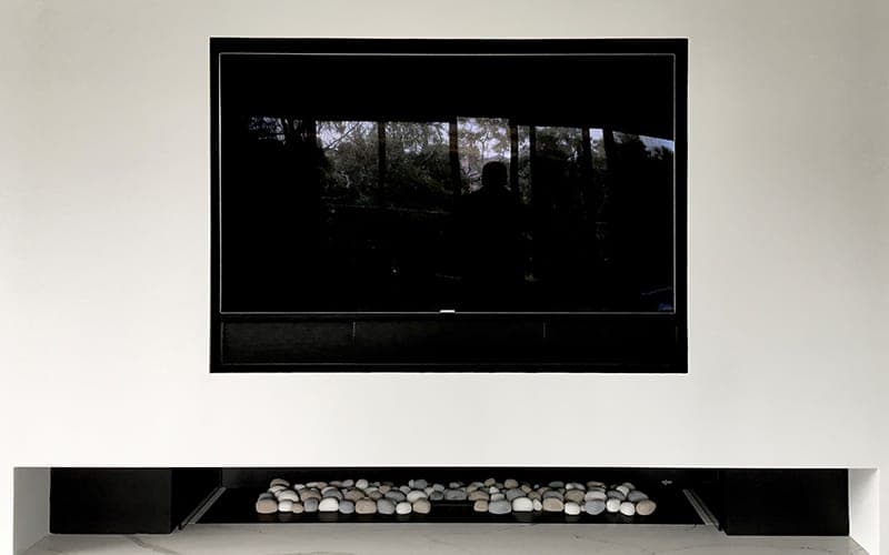 Large TV mounted above a fireplace in a white wall recess