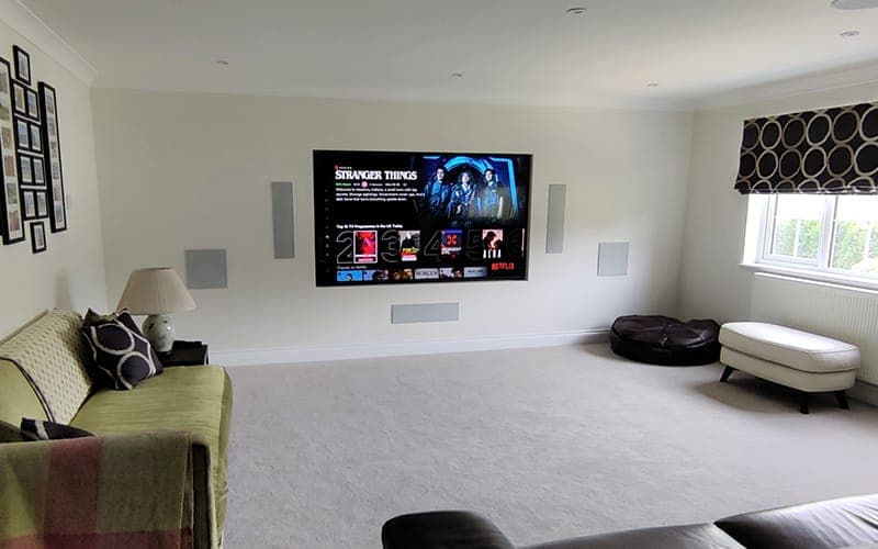 Home theatre in a carpeted lounge with a wall-mounted TV and in-wall speakers either side