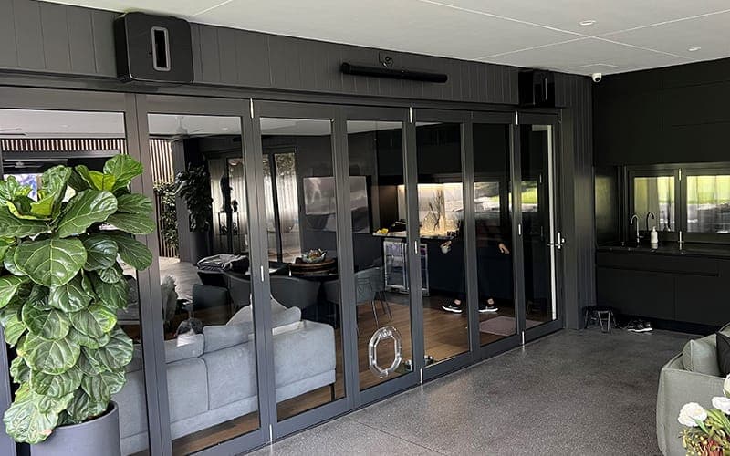 Outdoor speaker mounted on the corner of an alfresco area beside glass doors