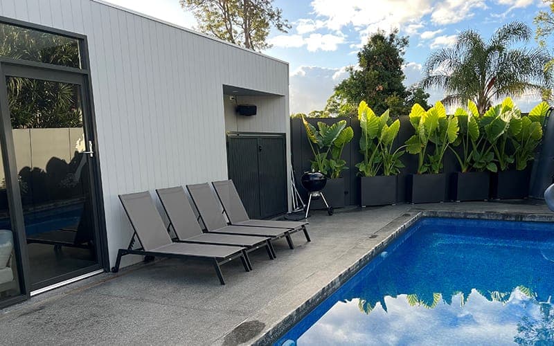 Outdoor speaker mounted on an external wall above a pool and sun lounges