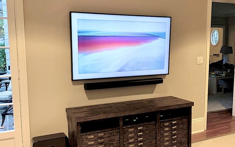 Frame-style TV with a soundbar mounted below it above a timber cabinet