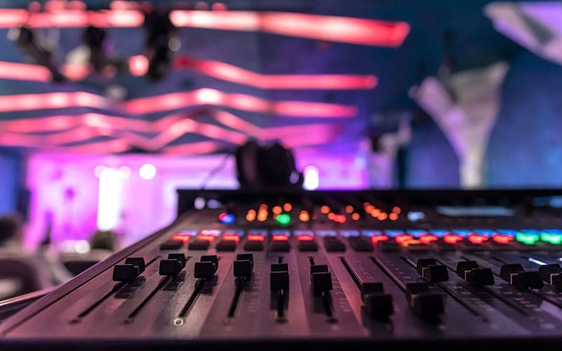 Audio mixing console at a live event, lit by stage lighting