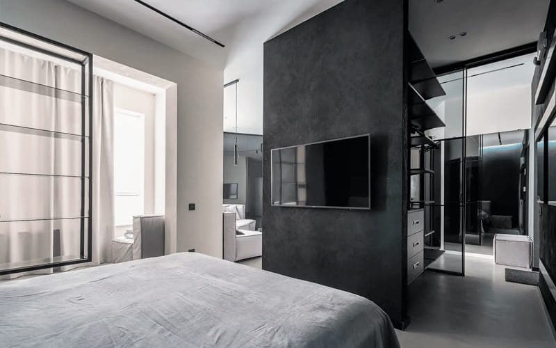 Wall-mounted TV on a dark textured feature wall dividing a bedroom from a walk-in wardrobe