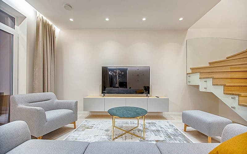 TV wall mounted above a low white media unit in a living room beside a timber staircase