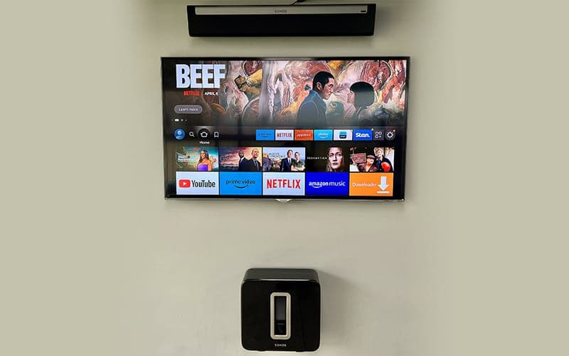 Wall-mounted smart TV with a soundbar above the screen and a wireless subwoofer below