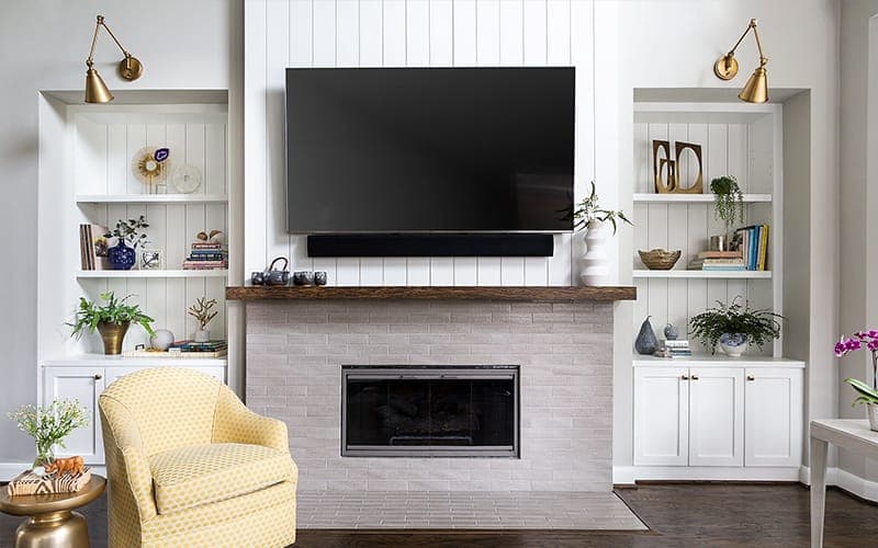 TV wall mounted above a fireplace between white built-in shelving, soundbar on the mantel