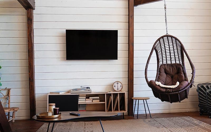 TV mounted on a white shiplap wall in a living room with a hanging chair