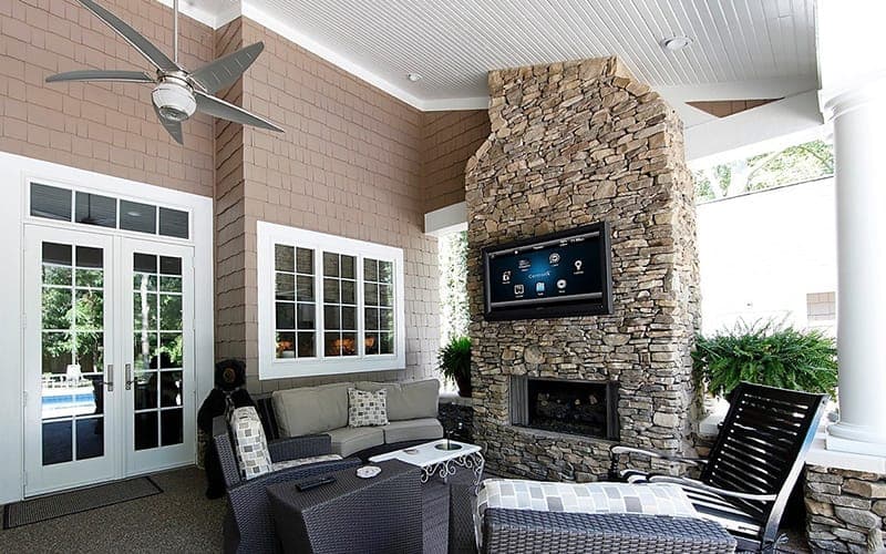 TV wall mounted on a stone chimney breast above a fireplace in a covered outdoor area
