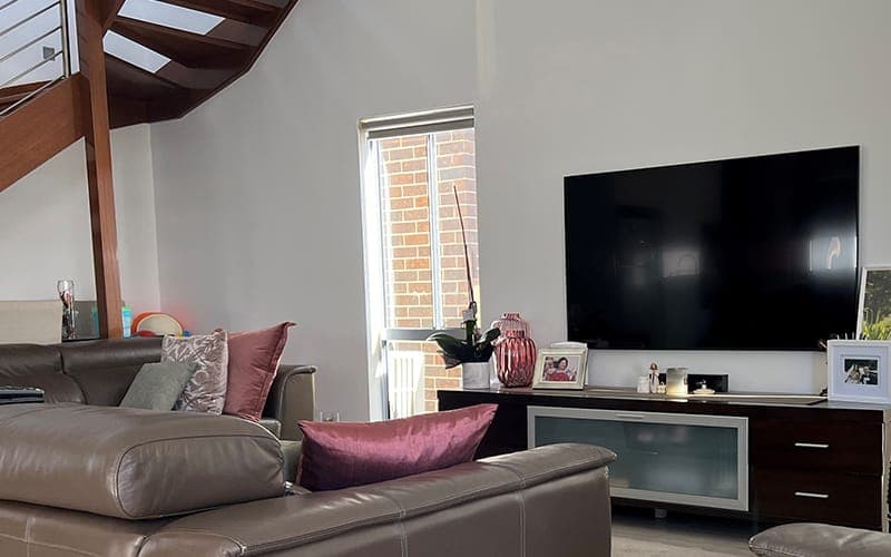 Large TV wall mounted in a double-height living room beside an open staircase