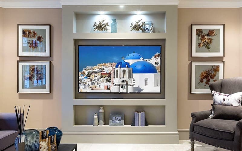 TV recessed into a lit wall niche between framed artwork in a formal lounge
