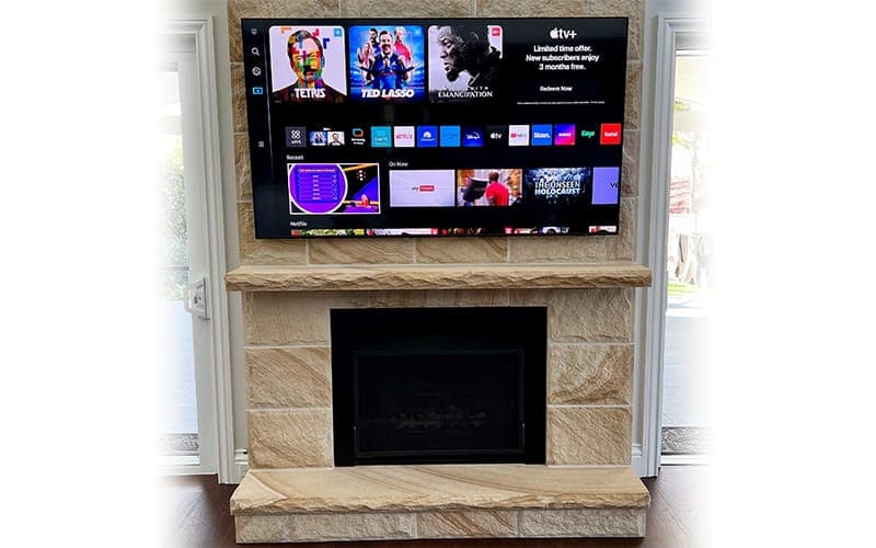 TV wall mounted above a sandstone fireplace with streaming apps on screen