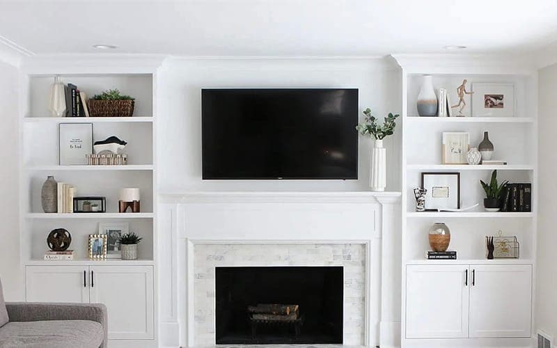 TV mounted above a fireplace between white built-in shelving in a Hamptons-style living room