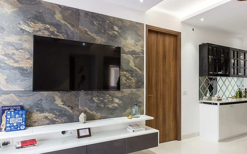 Large TV on a stone-tiled feature wall above a white floating shelf