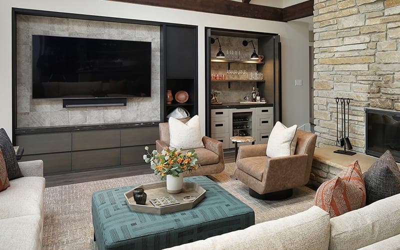 TV recessed into a concrete-look panel above a soundbar, beside a stone chimney and bar