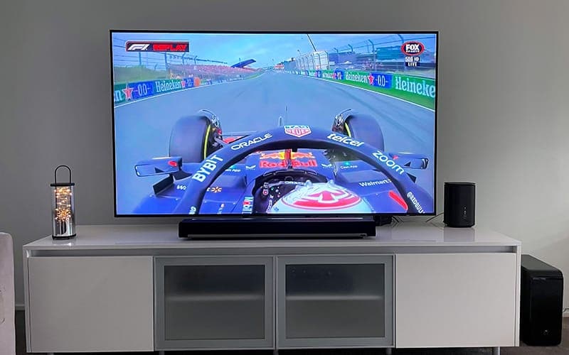 Wall-mounted TV showing Formula 1 on Fox Sports, with a soundbar and subwoofer below